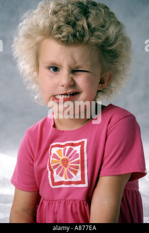 A cute little blond girl 4-6 year old wearing pink winking making a funny face pulling faces ugly fun mouth POV MR mugging funny humor humorous Stock Photo