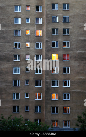 Vertical view of a large concrete apartment block Warsaw at night, featuring numerous windows with lights on against a dark, textured wall. Stock Photo