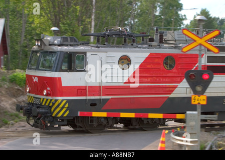 An electric locomotive passing railroad crossing ( Level-crossing or grade crossing ) boom down and red warning lights on , Finland Stock Photo