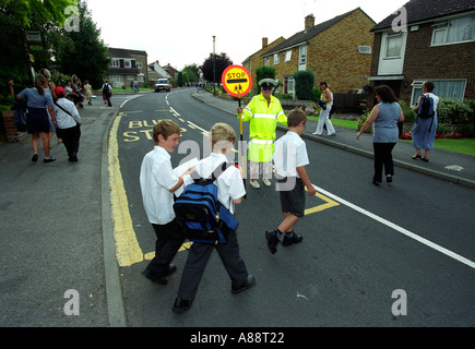 Children crossing the road with the assistance of lollypop lady after school day is over, Maidstone, Kent, UK. Stock Photo