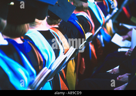 View of the backs of graduates wearing robes sitting in folding chairs at graduation Stock Photo