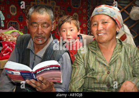 Nomads man woman and child are reading in the Lonely Planet guidebook in their yurte Kharkhiraa Mongolian Altai near Ulaangom Stock Photo