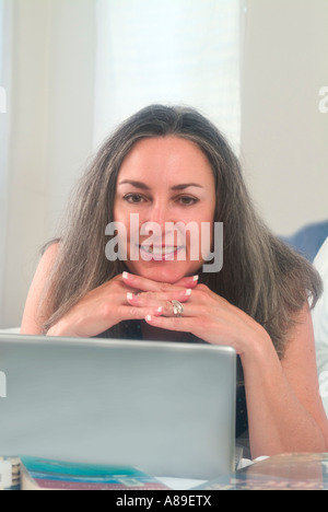 View of youthful smiling mature woman with long grey hair working on her laptop Stock Photo
