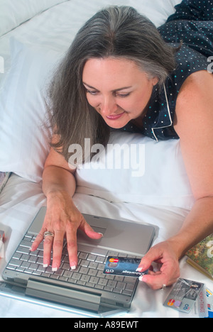 Mature woman with beautiful long grey hair using credit card and shoping online while lounging in bed Stock Photo