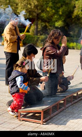 CHINA BEIJING Chinese Buddhists including a tiny girl toddler and her mother burn incense and kneel to pray Stock Photo