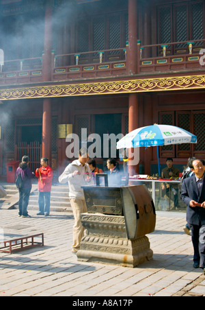 CHINA BEIJING Chinese Buddhists burn incense as tourists wander through the courtyard inside the Palace of Peace and Harmony Stock Photo