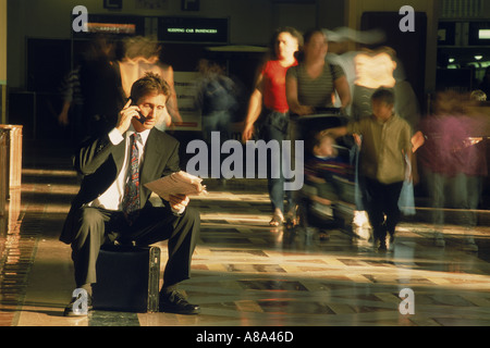 Businessman sitting on briefcase talking on cellphone and reading paper in Los Angeles Train Station Stock Photo