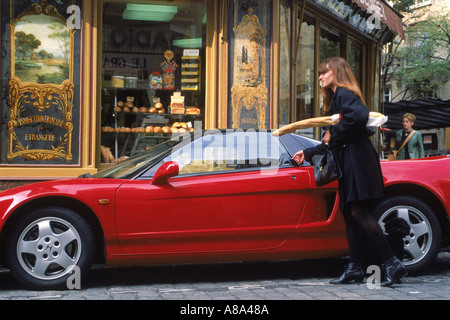 Woman leaving Boulangeria in Paris with baguette and French poodle opening door of  her super expensive red sports car Stock Photo
