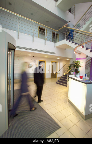 Reception desk in the foyer of an office building with blurred, smartly dressed people in suits entering via a revolving door. Stock Photo