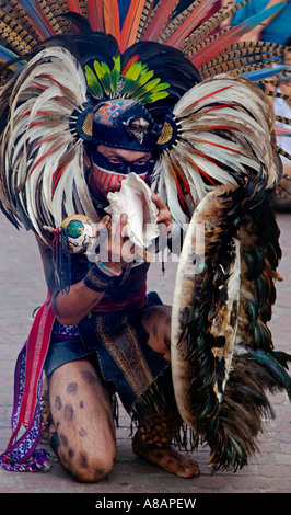 An AZTEC DANCER blows a CONCH in a traditional feathered warrior COSTUME during the CERVANTINO FESTIVAL GUANAJUATO MEXICO Stock Photo