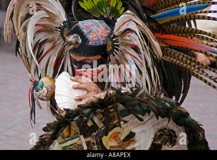 An AZTEC DANCER blows a CONCH in a traditional feathered warrior COSTUME during the CERVANTINO FESTIVAL GUANAJUATO MEXICO Stock Photo