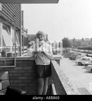 Black and white portrait of a young blonde woman on the balcony of a flat from 1969 with an leather chair Stock Photo