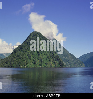 The steep pointed hill of Mitre Peak with white clouds over the top in the Fjord waters of Milford Sound New Zealand Stock Photo