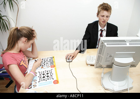 boy in school uniform sitting at a computer with sister reading girly magazine Stock Photo