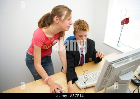 boy in school uniform sitting at a computer being helped by girl in casual dress Stock Photo