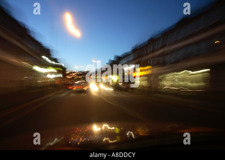 Seen through the windscreen of a car the street blurs as the vehicle speeds past shops and street lights South London UK Stock Photo