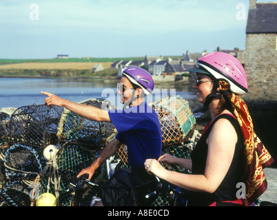 dh Two cyclists holiday ORKNEY  Cyclist helmet uk tourist cycle helmets scotland couple cycling sightseeing looking sight seeing bikes pointing bike Stock Photo