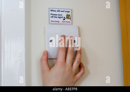 Hand turning off  light switch with energy saving sticker above UK Stock Photo
