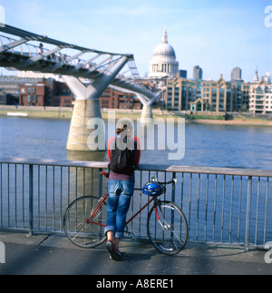 A man with bike bicycle cyclist standing watching the Thames River flow by the Millennium Bridge in City of London England UK KATHY DEWITT Stock Photo