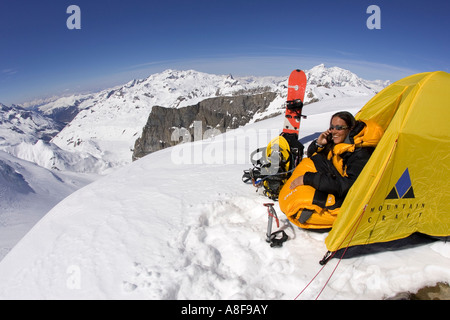 Female mountaineer makes cell / sat  phone call from camp in Alpine enviroment. Stock Photo