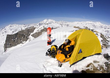 Female mountaineer on summit camped for the night with split snowboard. Stock Photo