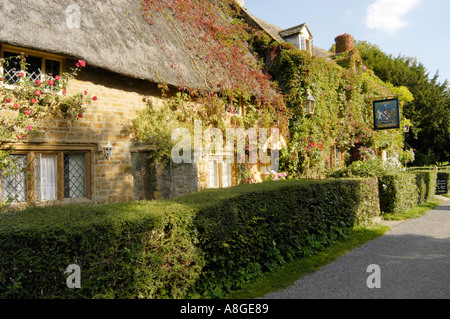 Traditional thatched cottage next door to the pub in the rural Cotswold village of Great Tew in Oxfordshire Stock Photo