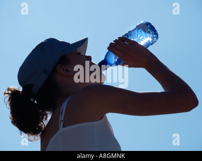 Silhouetted teenage girl drinking bottled mineral water against blue sky closeup Stock Photo