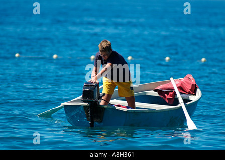 Young Boy in a Rowing Boat on the Sea Starting an Outboard Motor Stock Photo