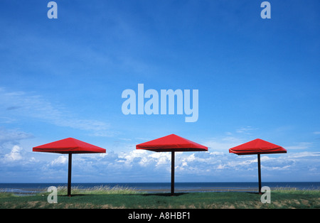 Three red beach umbrellas on the shore of the Bay of Chaleur New Brunswick Canada with storm clouds brewing in the distance Stock Photo