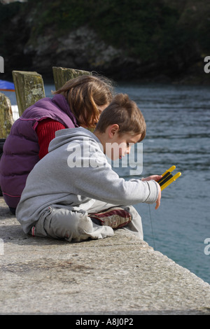 Children fishing for crabs on quayside at Looe Cornwall Stock Photo