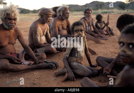 Aboriginal elders and young boys in ceremonial body paint sit on the red sand by fire after sunset in desert Central Australia Stock Photo