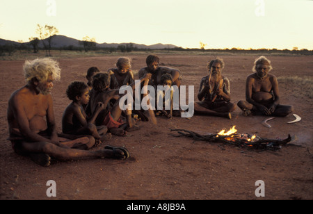 Aboriginal elders and young boys in ceremonial body paint sit on the red sand by fire after sunset in desert Central Australia Stock Photo