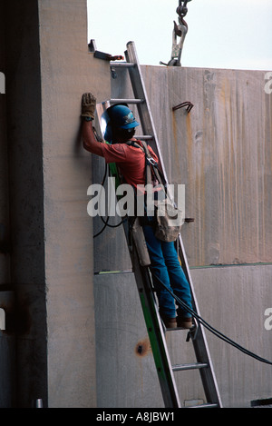 Masked man on ladder welding at construction site Stock Photo