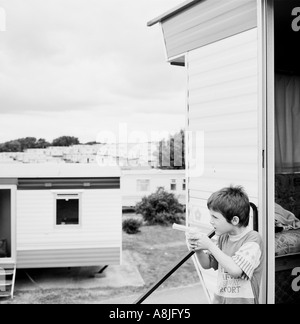 A boy plays with a water pistol on the steps of a caravan in a holiday park near Weymouth, Dorset. Stock Photo