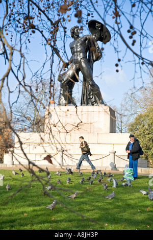 a man feeds birds next to a statue of Achilles in a London park Stock Photo