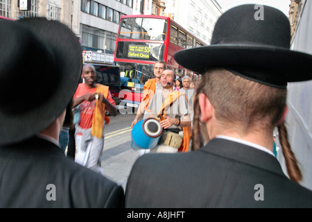 two orthodox jewish men walk past some Hare Krishnas on Oxford Street, London Stock Photo