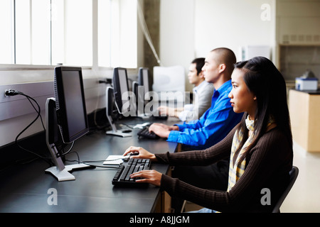 Side profile of a businesswoman and two businessmen sitting in an office and using computers Stock Photo