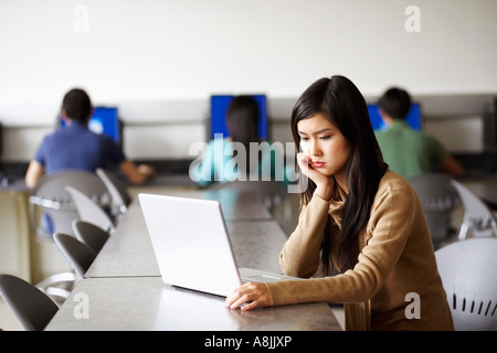 Side profile of a young woman sitting in front of a laptop and thinking