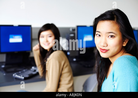 Portrait of two young women sitting in front of computers and smiling Stock Photo
