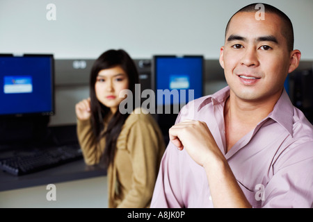 Portrait of a young man and a young woman sitting in front of computers and grinning Stock Photo