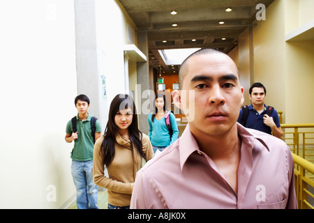 Portrait of a young man looking serious with two young women and two young men walking in the corridor behind him Stock Photo