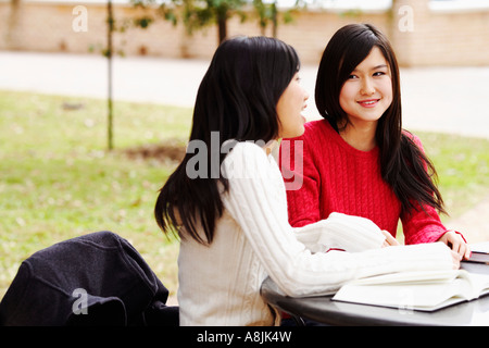 Two young women sitting in a college campus and talking to each other Stock Photo