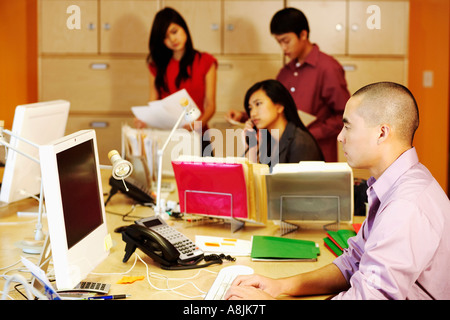 Side profile of a businessman using a computer in an office with two businesswomen and a businessman working in the background Stock Photo
