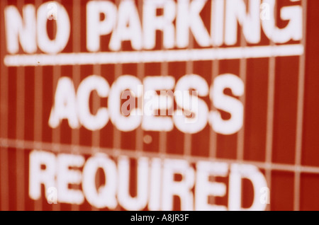Defocussed red and white sign behind builders or roadworks wire grill fence stating No parking Access required Stock Photo