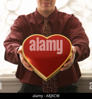 Mid adult Caucasian man holding a heart shaped box of chocolates at viewer Stock Photo