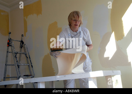 Woman DIY papering her room walls with lining paper. Stock Photo