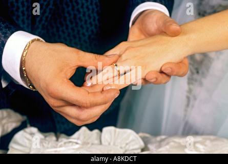 Groom places gold wedding ring on the finger of his new bride in marriage ceremony Stock Photo