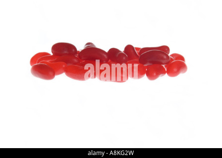 Horizontal close up of lots of identical red jelly beans on a white background. Stock Photo