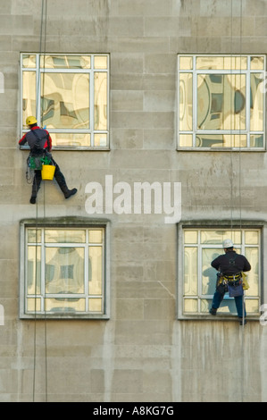 Vertical close up portrait of two window cleaners suspended from ropes high up on an office block. Stock Photo