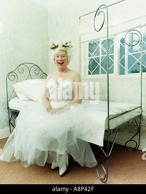 Elderly woman dressed in fairy costume sitting on edge of bed laughing Stock Photo